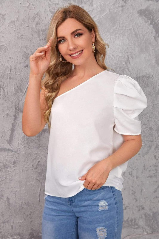 A woman wearing a white blouse with one puff sleeve, paired with blue jeans.