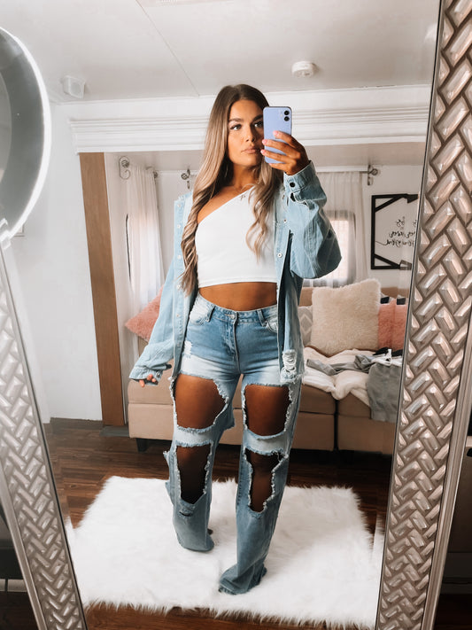 A person wearing a blue denim jacket and a white top taking a mirror selfie.