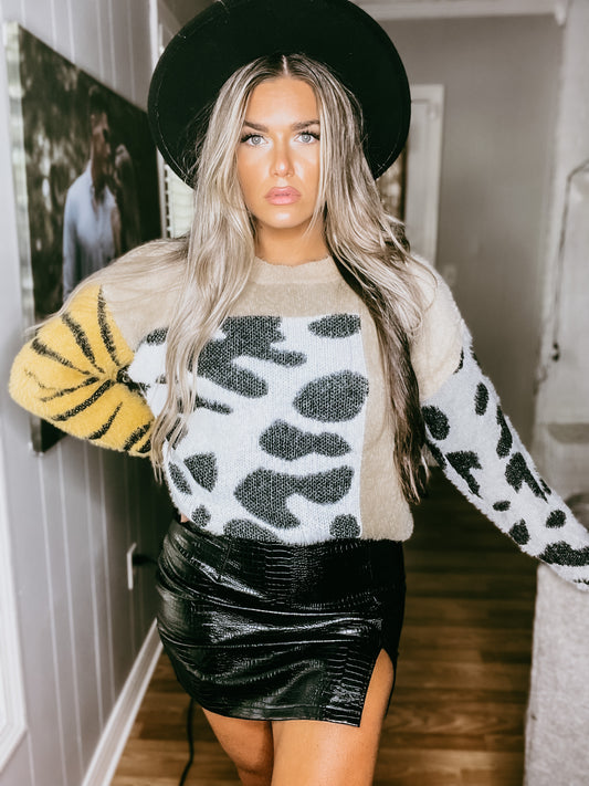 A woman wearing a crew neck sweater with leopard print pattern, paired with a black skirt and black boots.