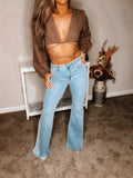 A person wearing brown-colored, flare-cut blue jeans and a brown, loose-fitting top. The jeans are frayed at the hem, indicating a stylish, distressed look.