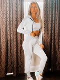 A woman wearing a gray 3-piece sports set including a top, leggings, and sports bra. The set is made from a soft and stretchy material.