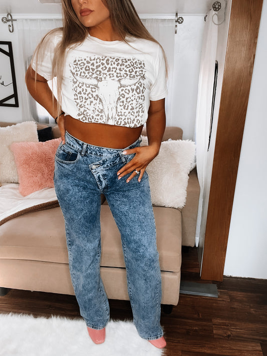 A person wearing a white top with a leopard print pattern and blue wide leg jeans.