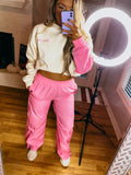 A person wearing pink parachute pants with a hoodie, standing in a room with a mirror and a light source overhead.