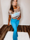 A woman wearing a blue, checkered sea-inspired top with three-quarter sleeves and a round neckline, paired with blue jeans.