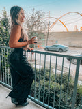 A person standing on a balcony wearing loose sparkle sequin black trousers with an elasticated waistband, paired with a black top and drinking from a glass.
