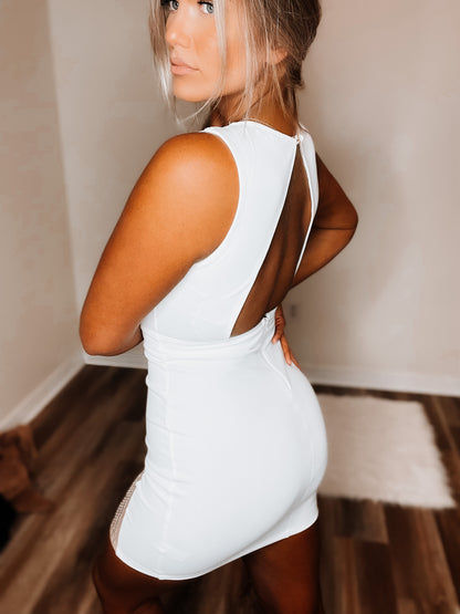 A woman posing in a white short dress with a high neckline and sleeveless top, showing the back of the dress standing in a room 