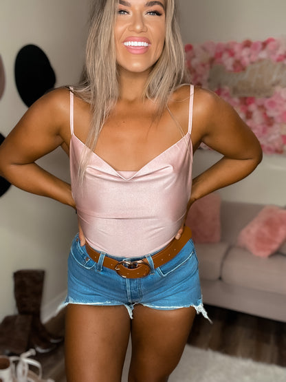 A woman wearing a pink silky bodysuit with a V-neck and sleeveless design, paired with blue denim shorts.